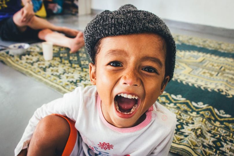 A young child wearing a black and white knitted hat crouched on a carpet with their mouth wide open.